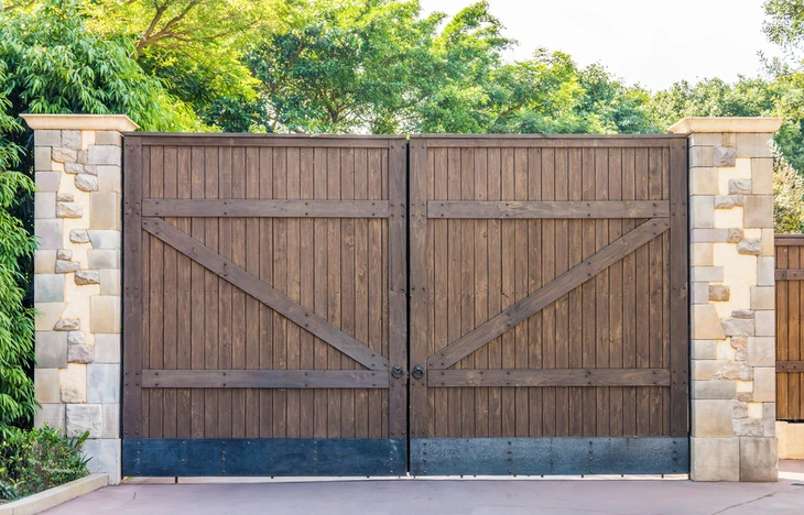 Portail extérieur résidentiel à double vantaux en bois naturel avec traverses diagonales, intégré dans clôture maçonnée