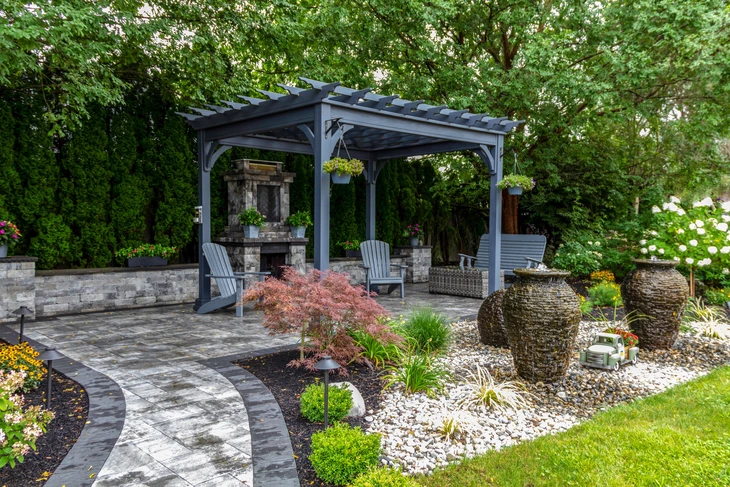 Grande pergola grise sur les pavés avec cheminée en pierre et des urnes de cascade pour la conception de paysage d'oasis de cour arrière