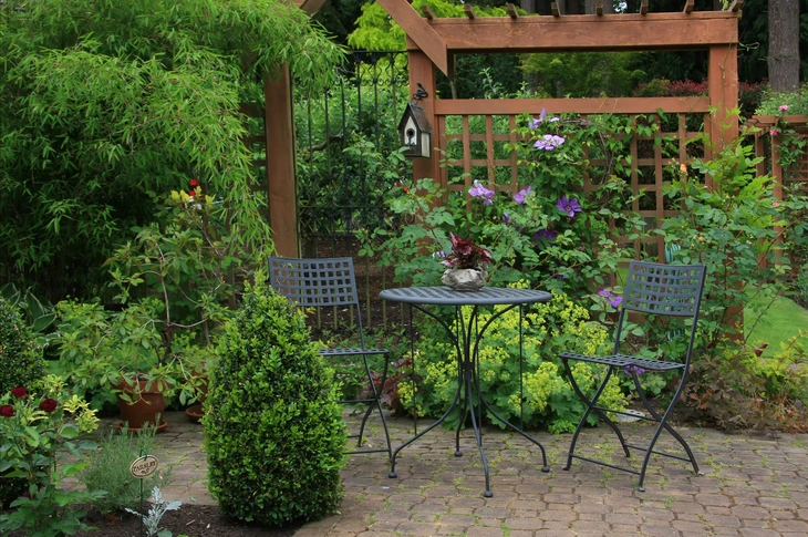 Jardin extérieur aménagé avec salon de jardin en fer forgé noir, table ronde et deux chaises à dossier ajouré sur terrasse pavée