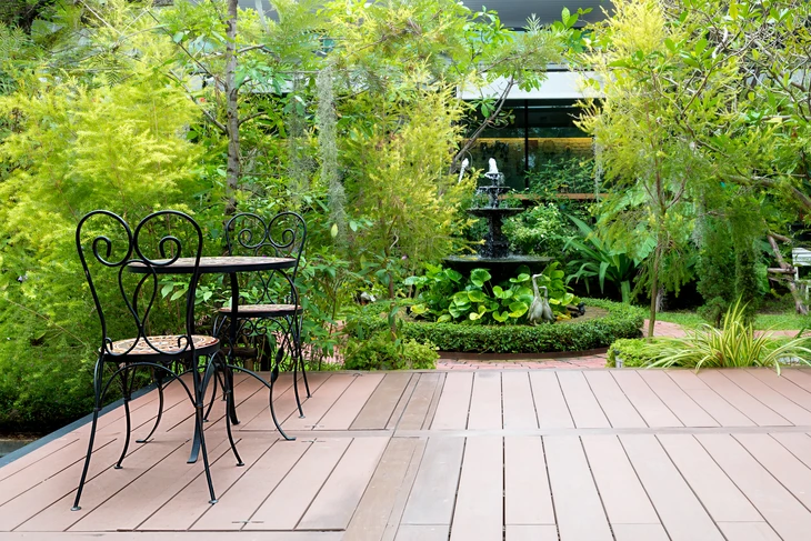 Terrasse extérieure avec mobilier de jardin en fer forgé noir, table et chaises à motifs spiralés sur plancher bois composite