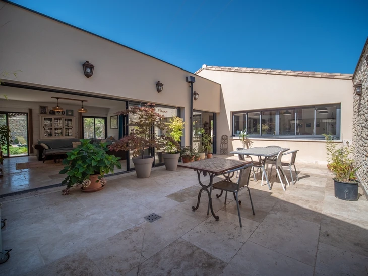 Terrasse extérieure couverte d'une maison contemporaine avec salon de jardin en fer forgé, nombreuses plantes en pots