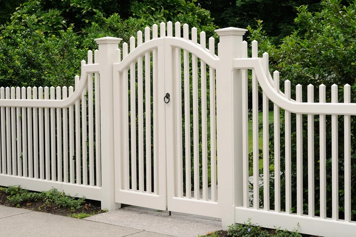 Scène extérieure résidentielle avec portail et clôture en PVC blanc installés dans un jardin paysagé