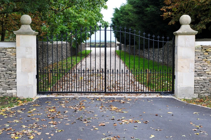 Entrée de propriété avec portail en fer forgé noir à barreaudage vertical et ornements décoratifs