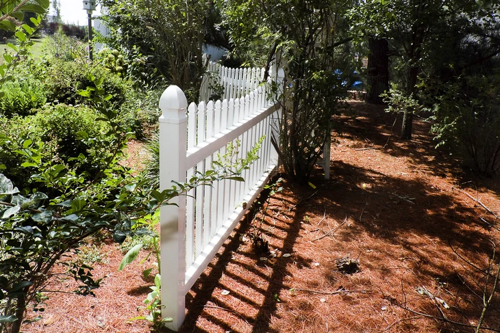 Extérieur résidentiel avec clôture en PVC blanc de style traditionnel à piquets verticaux, poteaux à têtes arrondies et traverse horizontale