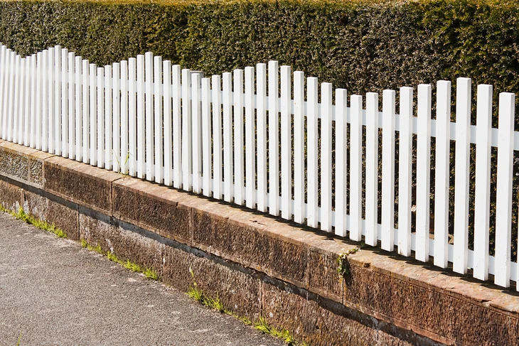 Clôture résidentielle extérieure avec palissade blanche en PVC ou bois peint, montée sur muret en béton avec chaperon brique