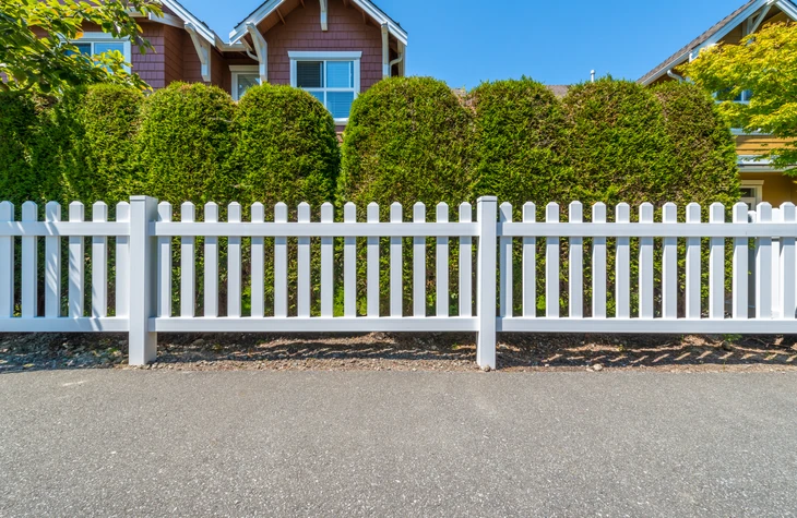Clôture résidentielle en PVC blanc de style palissade avec poteaux et traverses horizontales, délimitant une propriété suburbaine