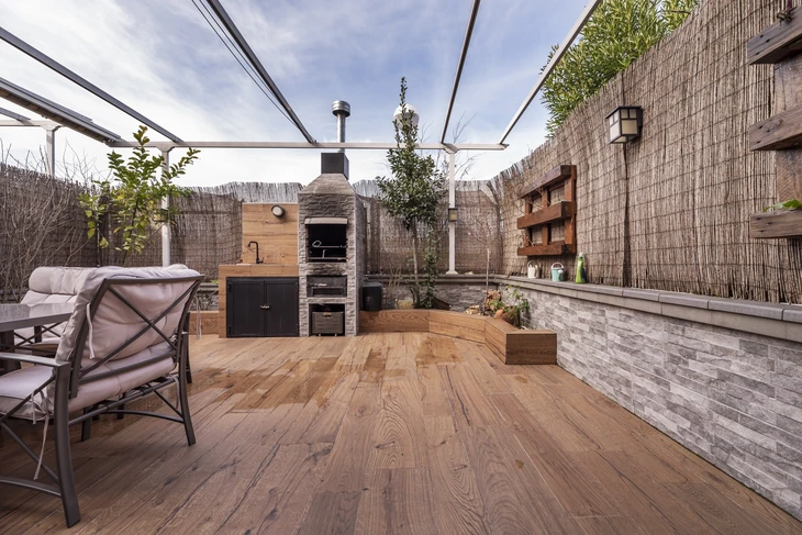 Terrasse extérieure couverte avec pergola vitrée, équipée d'un four à pizza en pierre avec cheminée métallique