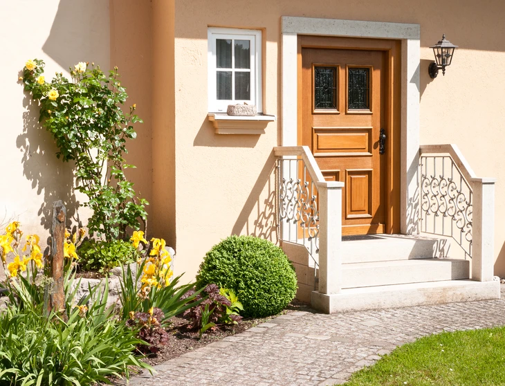 Entrée d'une maison résidentielle avec escalier en pierre, rampe décorative en fer forgé blanc et porte en bois massif à panneaux