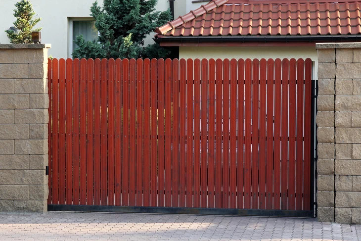Extérieur résidentiel avec portail coulissant en bois rouge-brun à lames verticales, intégré dans clôture en blocs de béton beige
