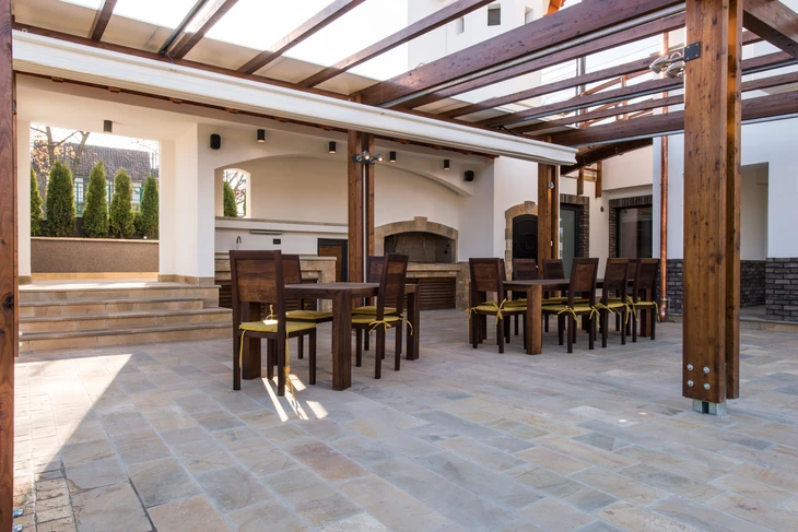 Terrasse couverte d'un restaurant avec pergola en bois, tables et chaises en bois foncé avec coussins jaunes