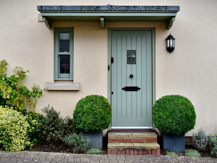 Entrée de maison résidentielle avec porte en bois vert olive, poignée et heurtoir noirs, fenêtre latérale assortie