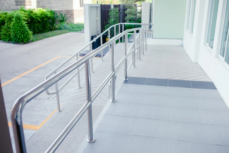 Rampe d'accès extérieure en acier inoxydable avec main courante double rail, installée devant l'entrée d'un bâtiment moderne