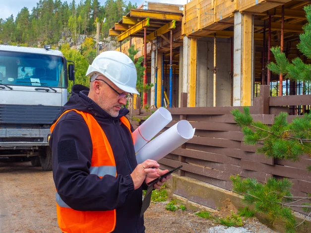 Chantier de construction extérieur avec ouvrier en équipement de sécurité consultant plans architecturaux et tablette numérique