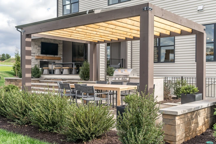 Terrasse extérieure aménagée avec pergola moderne en bois et acier, équipée d'un espace barbecue intégré et coin salon avec cheminée