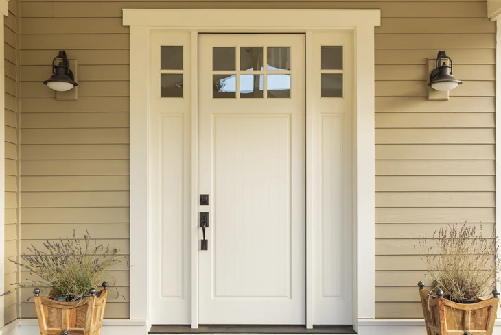 Entrée principale d'une maison avec porte blanche à panneaux et imposte vitrée, flanquée de baies latérales