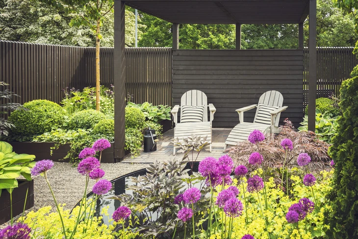Jardin paysager avec terrasse couverte, deux chaises Adirondack blanches sur gravier