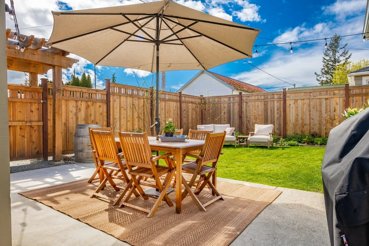 Terrasse extérieure résidentielle avec salon de jardin en teck comprenant table rectangulaire et chaises pliantes sous parasol déporté beige