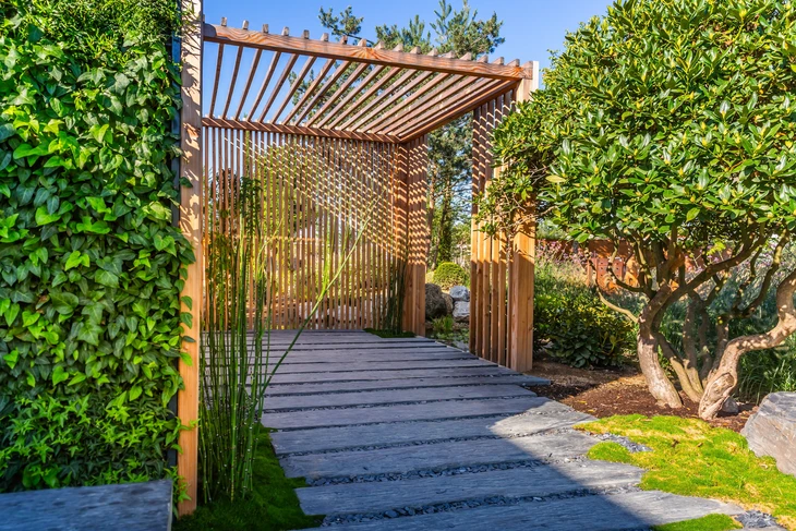 Jardin extérieur avec pergola en bois naturel à lames horizontales créant un passage couvert
