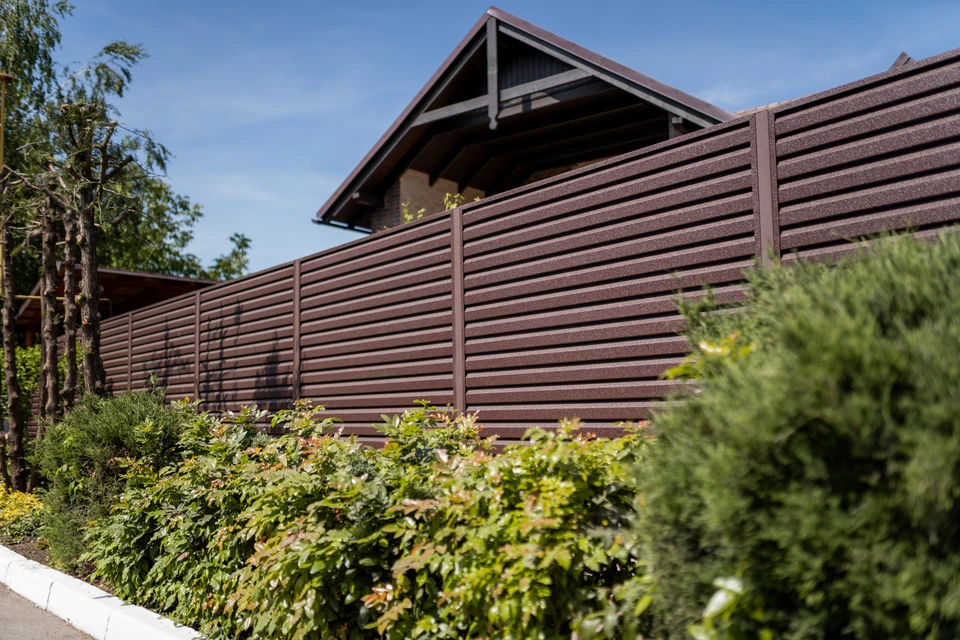 Scène extérieure résidentielle avec clôture moderne en lames horizontales brun foncé longeant une propriété