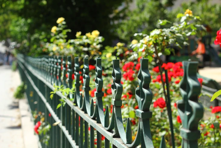 Scène extérieure d'un jardin public avec rambarde ornementale en fer forgé vert foncé longeant une allée