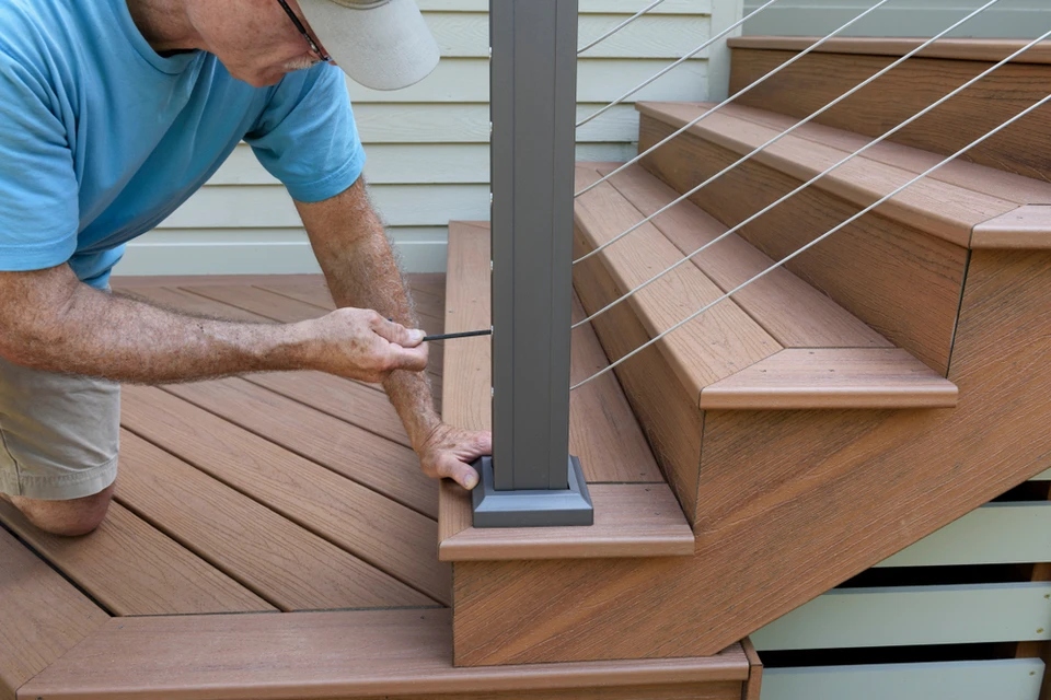 Homme en t-shirt bleu installant une rambarde sur terrasse en bois extérieure