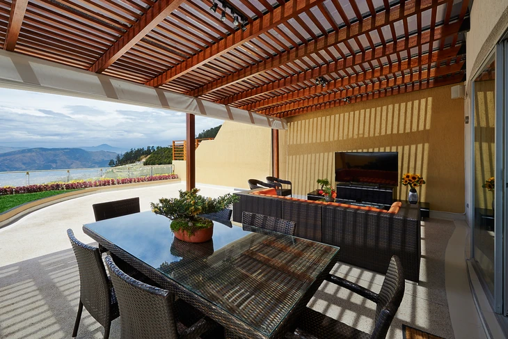 Terrasse extérieure couverte avec pergola en bois à lamelles, mobilier de jardin en résine tressée noire comprenant table et chaises, cuisine d'été avec plan de travail et barbecue intégré