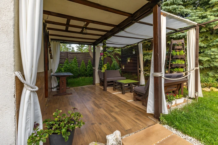 Terrasse extérieure aménagée sous pergola en bois avec toiture textile beige et rideaux blancs noués par cordage maritime