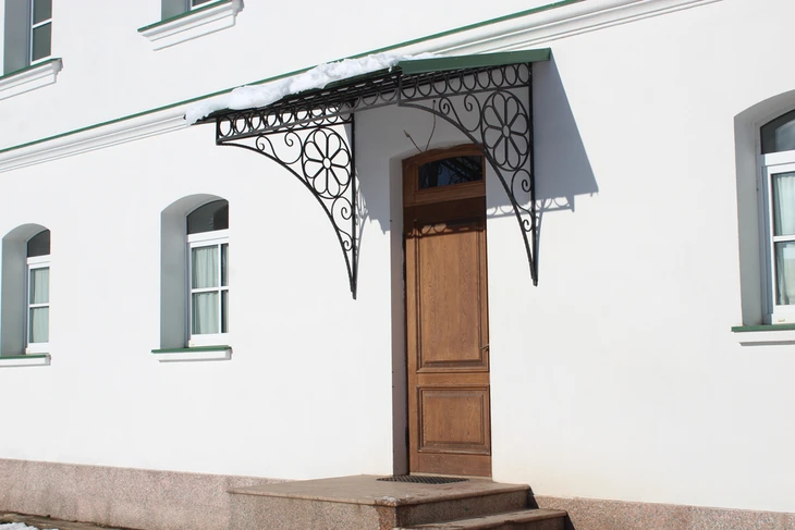 Façade blanche d'un bâtiment avec porte d'entrée en bois à double panneau et marquise en fer forgé ornementée