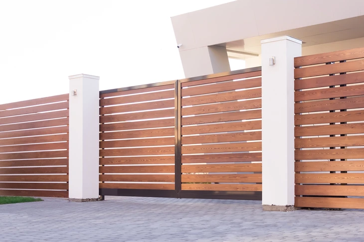 Portail et clôture moderne en bois exotique avec lames horizontales ajourées, piliers en béton blanc, finition contemporaine pour propriété résidentielle
