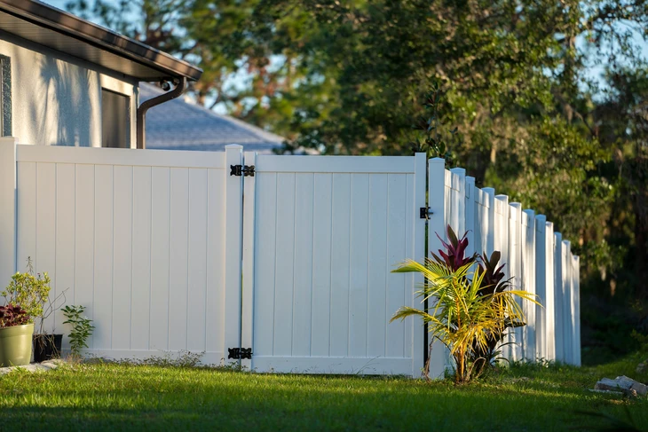 Jardin résidentiel avec clôture en PVC blanc à lames verticales, portillon d'accès avec charnières noires