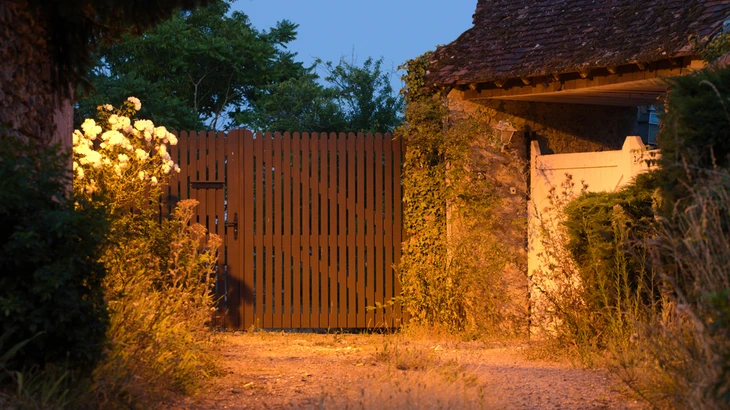 Entrée de propriété rustique au crépuscule avec portail en bois à lames verticales, éclairage d'ambiance chaleureux