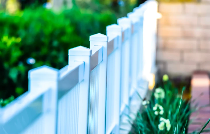 Clôture résidentielle blanche en PVC ou vinyl avec poteaux carrés et panneaux verticaux installée le long d'un chemin pavé