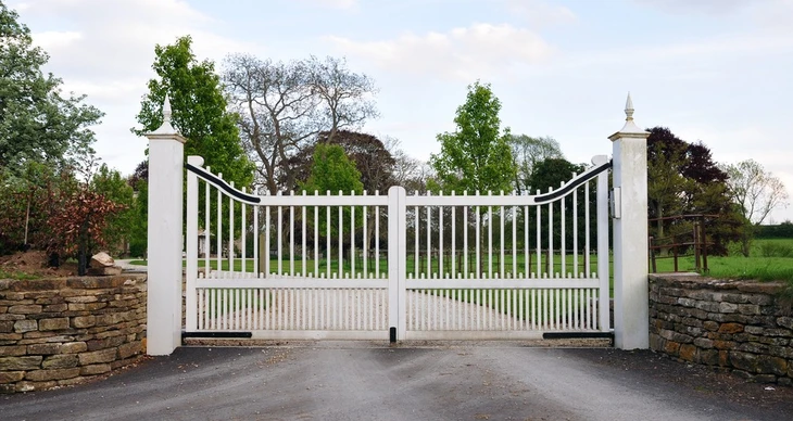 Portail d'entrée extérieur résidentiel en métal blanc à double battant avec barreaudage vertical décoratif, installé entre piliers maçonnés et murets en pierre naturelle
