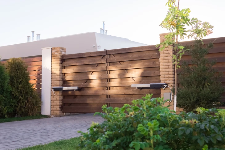 Portail contemporain à double vantaux en bois horizontal avec piliers en briques, intégré dans clôture assortie
