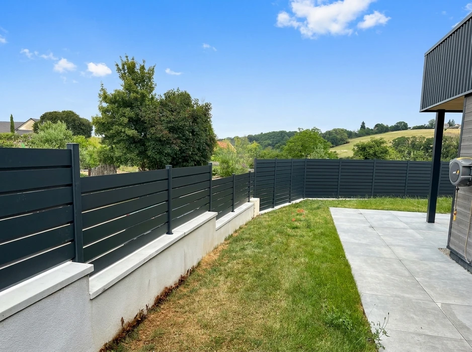 Jardin résidentiel moderne avec clôture aluminium anthracite à lames horizontales, montée sur muret béton enduit blanc