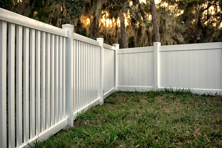 Clôture résidentielle en PVC blanc installée dans un jardin extérieur avec pelouse verte et arbres en arrière-plan
