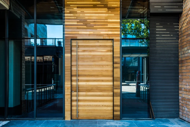 Entrée moderne d'immeuble résidentiel avec porte d'accès principale en bois massif à lames horizontales