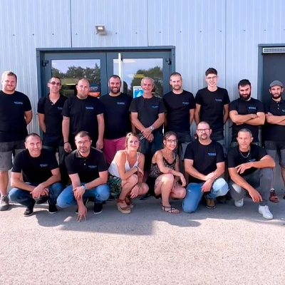 Scène extérieure, trois techniciens en tenue noire manœuvrent un châssis vitré de grande dimension à cadre rouge, positionné sur palette métallique CMU 1T500