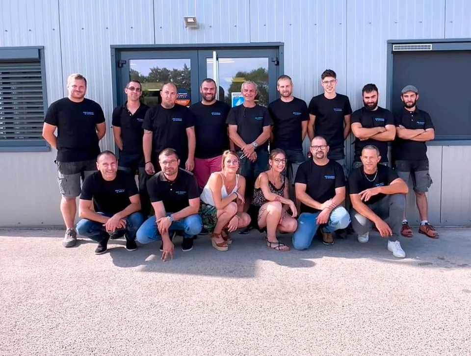 Groupe de 15 professionnels posant devant un bâtiment industriel, en deux rangées