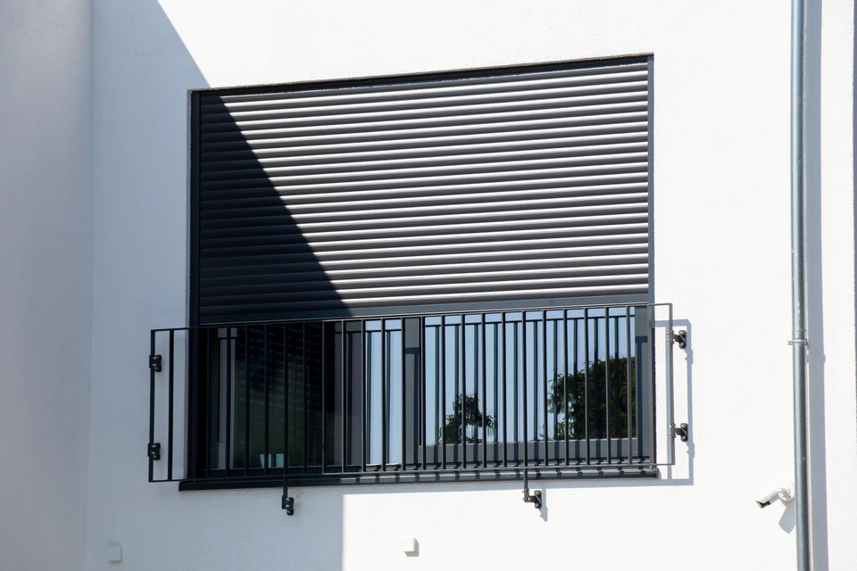 Façade moderne d'habitation avec volets roulants métalliques partiellement ouverts, terrasse en bois composite, éclairage extérieur LED intégré