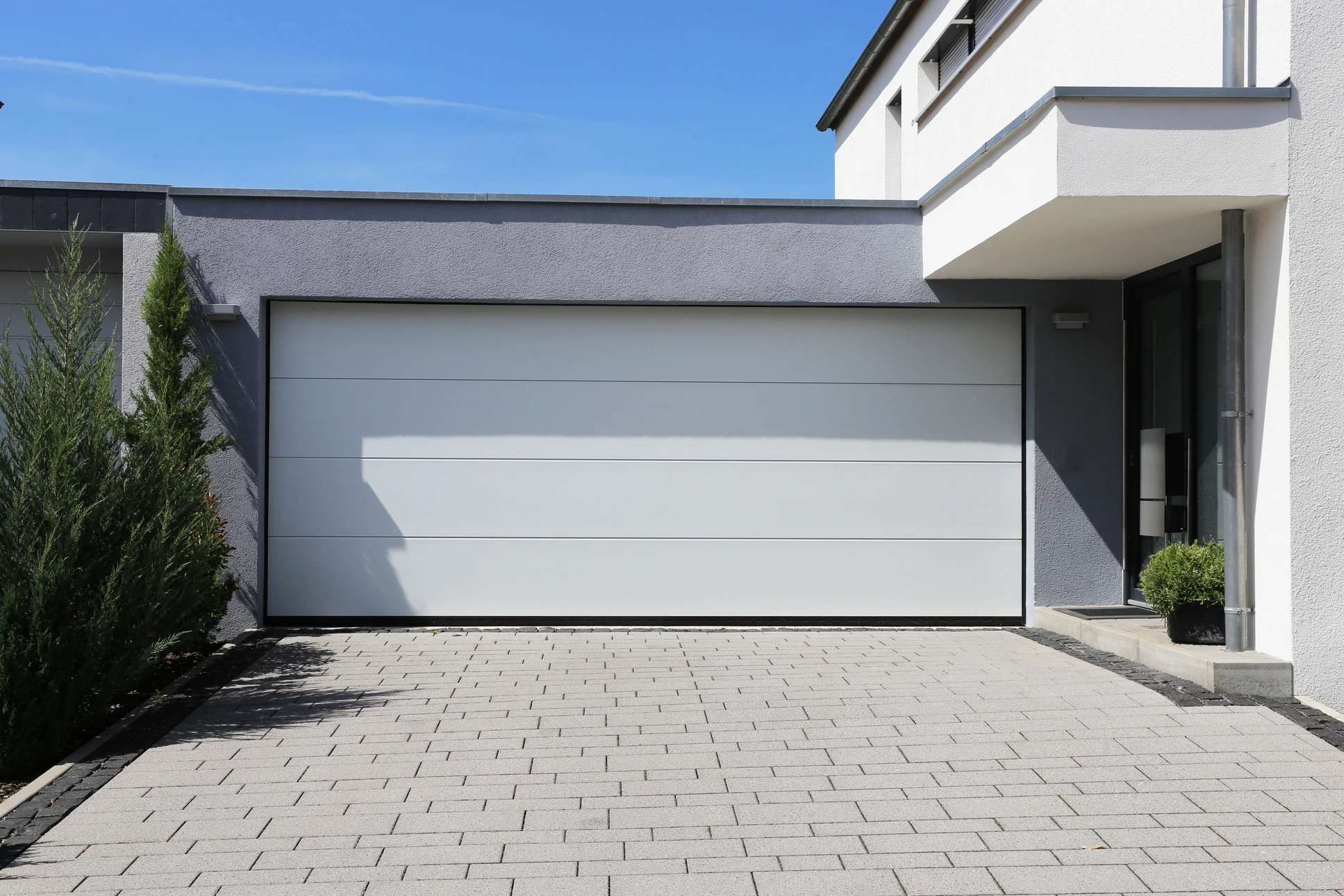 Façade extérieure d'un garage résidentiel à deux places avec portes sectionnelles blanches à panneaux rectangulaires et hublots décoratifs semi-circulaires
