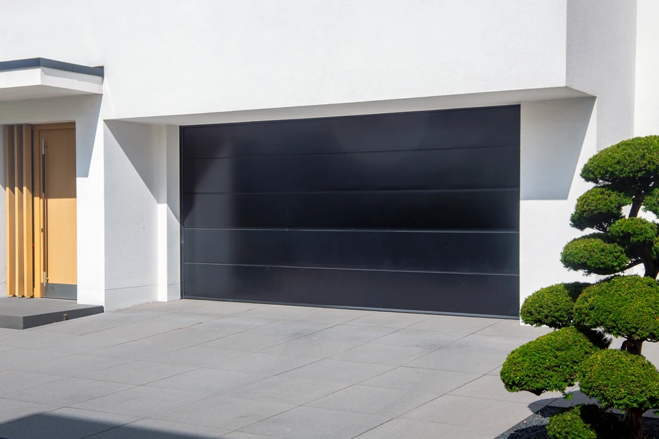 Garage résidentiel avec porte sectionnelle blanche partiellement ouverte, façade en bardage bois peint beige, toiture à pignon avec bardeaux d'asphalte