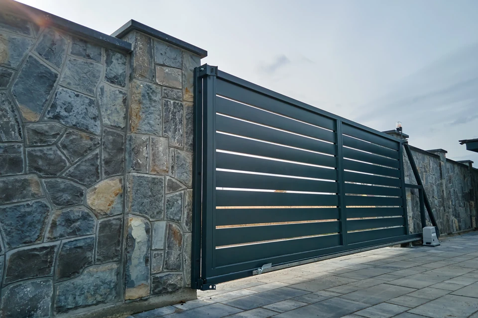 Entrée résidentielle avec portail coulissant automatique en aluminium anthracite à lames horizontales, intégré dans clôture maçonnée blanc cassé avec piliers béton